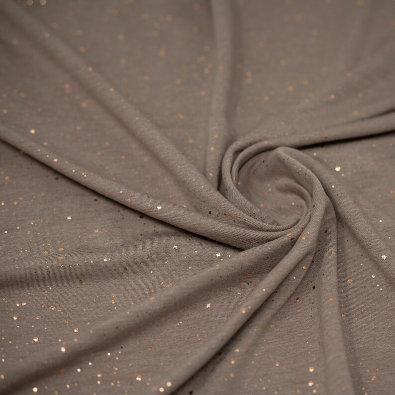 May include: A close-up of a gray fabric with a subtle shimmer of gold glitter. The fabric is soft and has a slightly textured surface.