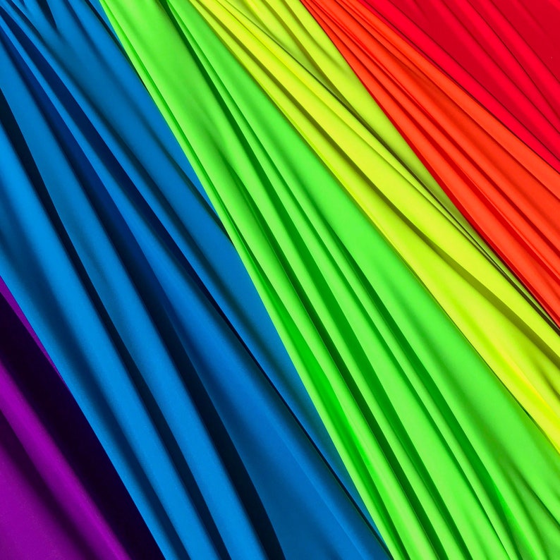 May include: A close-up of fabric swatches in a rainbow of colors, including purple, blue, green, yellow, orange, and red. The fabric is folded and draped, creating a textured and colorful background.