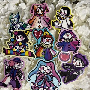 Peut inclure: Collection de neuf autocollants de clowns colorés dans diverses poses. Chaque autocollant présente un design de clown différent avec des couleurs vives, dont le rose, le bleu, le jaune et le violet. Les autocollants sont posés sur un fond de fleurs blanches.