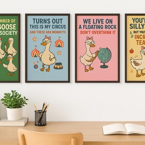 May include: Four framed art prints with goose illustrations and humorous text. The prints feature geese with glasses and bows, circus imagery, and motivational phrases. The frames are dark brown, and the prints are displayed on a wooden desk.