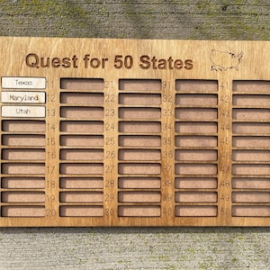 May include: A wooden board with 50 numbered slots for collecting state-themed items. The board is labeled "Quest for 50 States" and features a small outline of the United States. The slots are labeled with numbers 1 through 50. The first three slots have labels for Texas, Maryland, and Utah.