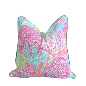 May include: Decorative throw pillow with a vibrant coral reef pattern in shades of pink, turquoise, and orange. The pillow has a teal blue border and a white background. The pillow is square-shaped.
