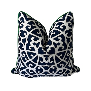 May include: Decorative throw pillow with a navy blue and white geometric pattern. The pillow has a green trim and is square-shaped. The pattern is a repeating design of swirling shapes. This pillow is suitable for a living room or bedroom.