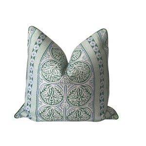 May include: A decorative square pillow with a white background and a repeating pattern of green leaves and circles. The pillow has a green border and a soft, inviting appearance.