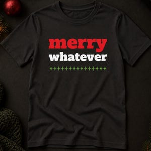 Pode incluir: Uma t-shirt preta de manga curta com o texto "merry" em vermelho e "whatever" em branco, posicionado acima de uma linha horizontal de pequenos ícones de estrelas verdes de quatro pontas. A t-shirt tem gola redonda e bainha reta.