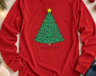 May include: A red long-sleeve shirt featuring a graphic of a green Christmas tree decorated with colorful string lights and a yellow star on top. Below the tree, the text "Too Lit to Quit" is printed in a simple black font on the fabric.