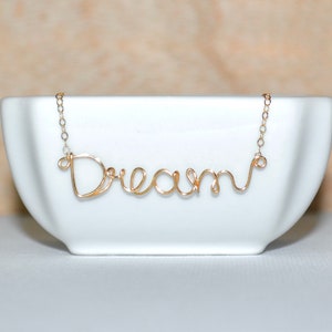 May include: Gold wire necklace with the word "Dream" spelled out in cursive.