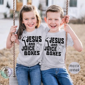 May include: Two children wearing gray t-shirts with the text "Jesus and Juice Boxes" and a cross graphic. The children are sitting on a swing set.