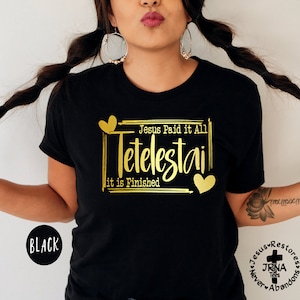 May include: Black t-shirt with gold lettering that reads "Jesus Paid it All Tetelestai it is Finished". The lettering is in a script font and is surrounded by a gold frame. There are two gold hearts on either side of the lettering.