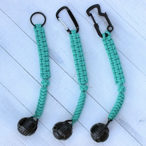 May include: Three teal paracord keychains with black accents. Each keychain features a woven cord, a black ball-shaped end, and a different attachment: a keyring, a carabiner clip, and a bottle opener clip.