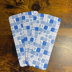 May include: A stack of blue and white patterned playing cards. Each card features a checkerboard design with seashell and floral illustrations. The cards are arranged on a dark wooden surface.