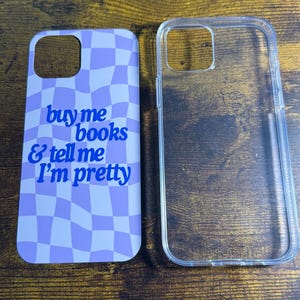Peut inclure: Un étui de téléphone transparent à côté d'un étui de téléphone avec un motif à carreaux violets et blancs. L'étui à motifs porte le texte "buy me books & tell me I'm pretty" en bleu.