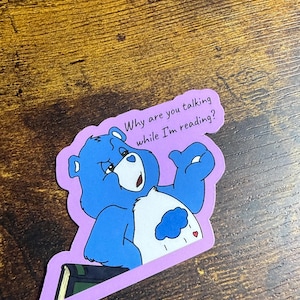 May include: A white ceramic mug with a black handle and the text "But First, Coffee" in a black, bold font. The mug is sitting on a wooden surface. The mug is approximately 4 inches tall.