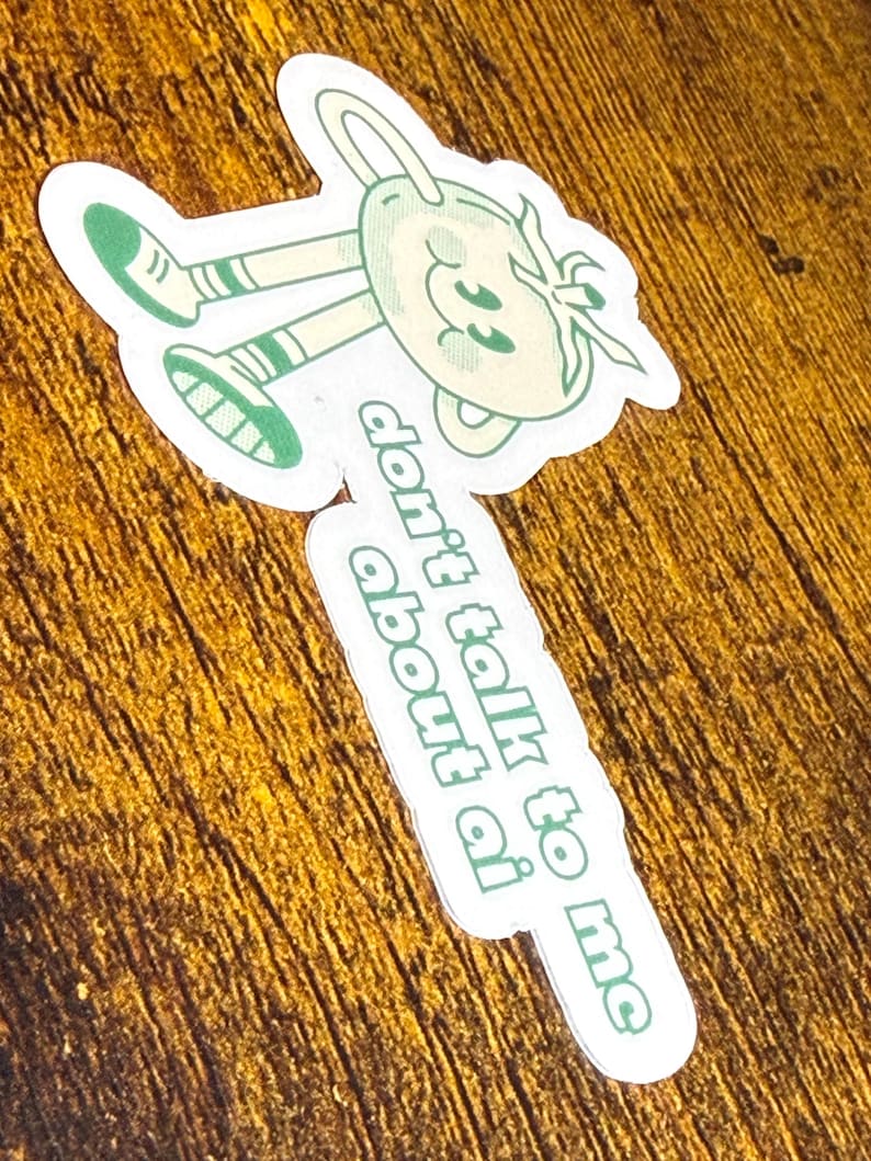 May include: A die-cut sticker featuring a cartoon character with a smiling face and limbs, wearing green shoes and striped socks. The sticker has the text "don't talk to me about ai" in green. The character is light green and white.
