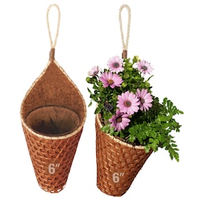 May include: Two hanging cone-shaped planters made of woven brown material. One planter is empty, and the other is filled with green foliage and purple flowers. Each planter has a 6-inch diameter and a rope handle.