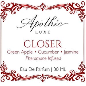 K&ouml;nnte beinhalten: Ein wei&szlig;es Etikett mit burgunderfarbenen Zierbl&uuml;ten und Text. Das Etikett lautet "Apothic LUXE CLOSER" mit Duftnoten von gr&uuml;nem Apfel, Gurke und Jasmin. Es ist ein Pheromon-infundiertes Eau De Parfum, 30 ml.