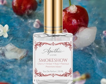May include: A perfume bottle with a gold cap and a label that reads "Apothic Luxe SMOKESHOW." The scent is described as cherry, amber, rose, and patchouli, with pheromones. The bottle is 30 ML. The background includes cherries and ice.