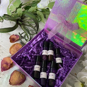May include: A purple gift box filled with purple tissue paper and six small glass bottles with black roll-on tops. The bottles are labeled "Apothecary Wine" and have different scents.