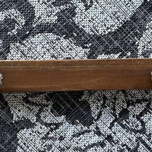 May include: A brown wooden shelf with two white and black ceramic knobs. The shelf is against a black and white patterned background.