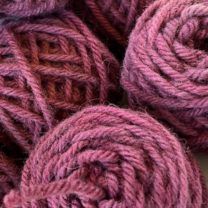 May include: Close-up of several balls of deep purple yarn. The yarn is soft and fluffy, and the balls are tightly wound.