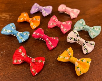 May include: Ten colorful hair bows with floral patterns. The bows are made of ribbon and have a metal clip on the back.