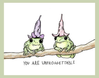 May include: Two green frogs wearing purple and pink flower hats are sitting on a branch. The text "You are Unforgettable" is written below the frogs.