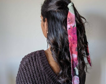May include: A woman with long, dark brown hair tied back with a pink and green floral patterned scarf.