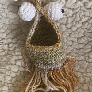 May include: A crocheted green and brown hanging pouch with white crocheted eyes and a fringe of brown and white yarn.