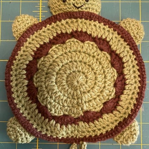 May include: A crocheted turtle toy with a brown and green shell and a brown head. The turtle has a small tail and four legs.