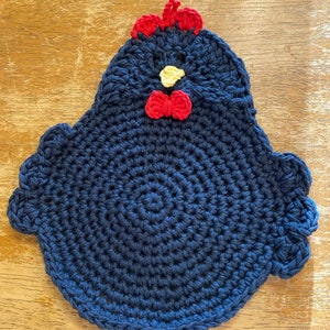 May include: A blue crocheted chicken pot holder with red and yellow accents. The chicken has a red bow tie and a yellow beak.