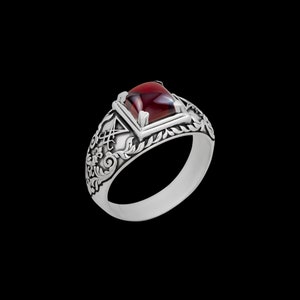 May include: A silver ring with an ornate design and a red gemstone. The ring features a square-shaped stone set in a silver bezel.