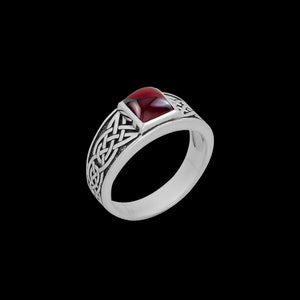 Puede incluir: Un anillo de plata con una piedra preciosa roja engastada en un diseño de nudo celta.