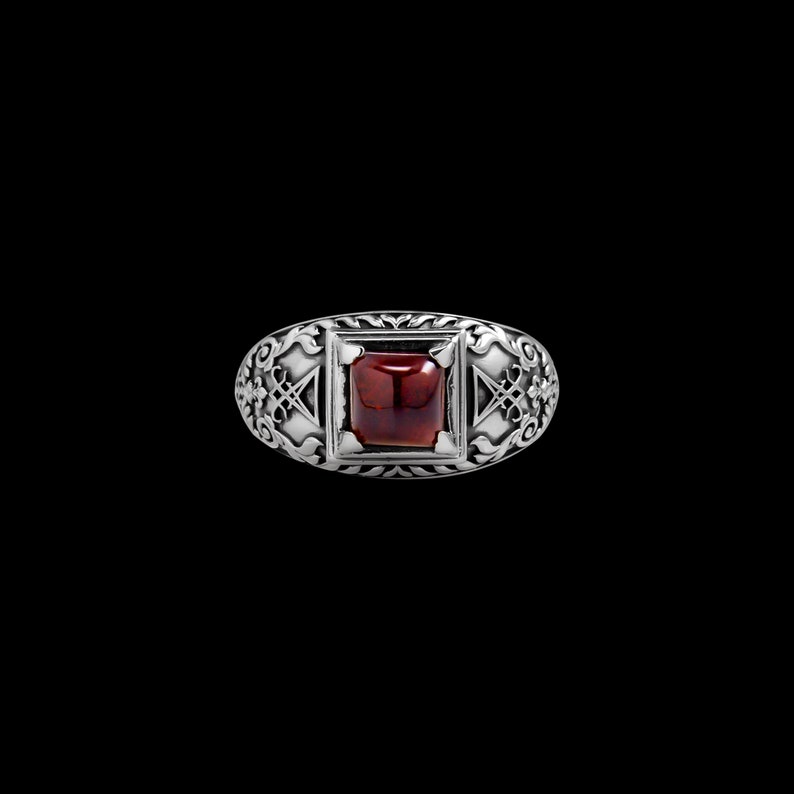 May include: A silver ring with an ornate design and a red gemstone in the center.