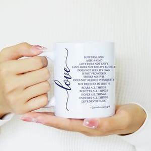 May include: A white ceramic mug featuring the word Love in a dark blue script font and the text of 1 Corinthians 13:4-8 in dark blue lettering. The text reads: Suffers long and is kind, love does not envy, love does not behave rudely, does not seek its own, is not provoked, thinks no evil, does not rejoice in iniquity, but rejoices in truth, bears all things, believes all things, hopes all things, endures all things, love never fails.
