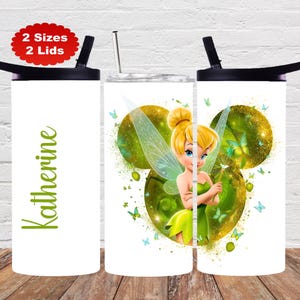 May include: A white cylindrical tumbler with a black lid and a straw, featuring the name Katherine in green script and a graphic of a blonde fairy with wings, green dress, and a wand, surrounded by golden circles and small blue butterflies.