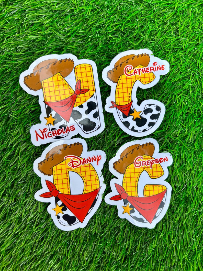 May include: Four custom stickers with a cowboy theme. Each sticker features a letter, a cowboy hat, a red bandana, and a cow-print design. The names "Nicholas", "Catherine", "Danny", and "Greyson" are printed on the stickers.