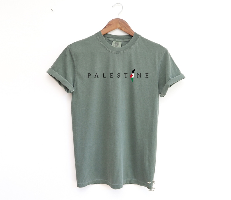 May include: A green t-shirt with the word "PALESTINE" printed in black letters and a silhouette of the Palestinian flag.
