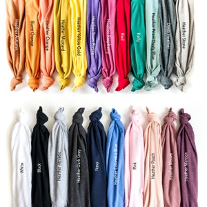 May include: A collection of folded t-shirts in various colors, including white, black, navy, and pink. Each shirt displays a color name, such as "Heather Autumn," "Heather Peach," and "Red." The shirts are arranged against a white background.