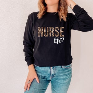 K&ouml;nnte beinhalten: Schwarzes Langarmshirt mit einem Leopardenmuster "NURSE life"-Aufdruck.