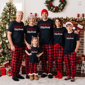 May include: A family of six wearing matching black t-shirts with "Merry Christmas" in white script and red and black plaid pajama pants. A Christmas tree and fireplace are in the background.