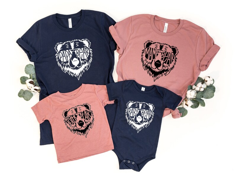May include: A collection of matching family t-shirts and a onesie. The shirts are navy blue and dusty rose, with a white bear graphic that says "Papa Bear," "Mama Bear," "Sister Bear," and "Baby Bear." The onesie is navy blue.