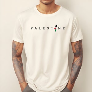 May include: White t-shirt with the word "PALESTINE" printed in black letters and a black, white, red, and green outline of the country of Palestine.