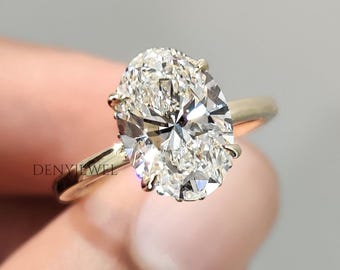 May include: A gold ring featuring a large, oval-cut diamond. The diamond sparkles with numerous facets, reflecting light. The ring's band is a simple, polished gold. The ring is held up by a hand.