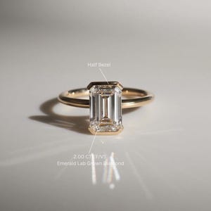 Puede incluir: Un anillo de oro con un diamante de laboratorio de talla esmeralda de 2,00 quilates engastado en una media engaste. El diamante es claro y tiene un brillo brillante. El anillo es simple y elegante.