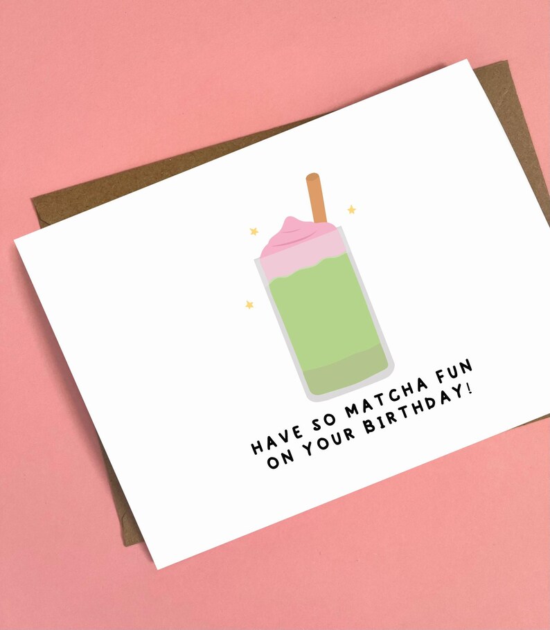 May include: A white greeting card with a matcha drink illustration. The drink is green with a pink topping and a brown stick. The card reads "HAVE SO MATCHA FUN ON YOUR BIRTHDAY!" on a pink background.