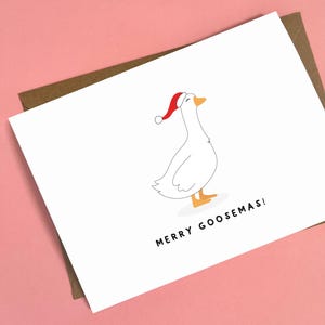 May include: A white greeting card with a cartoon goose wearing a red Santa hat. The card has the text "MERRY GOOSEMAS!" in black. The card is on a pink background with a brown envelope.
