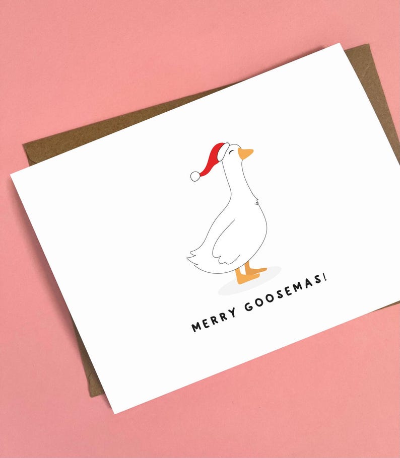 May include: A white greeting card with a cartoon goose wearing a red Santa hat. The card has the text "MERRY GOOSEMAS!" in black. The card is on a pink background with a brown envelope.