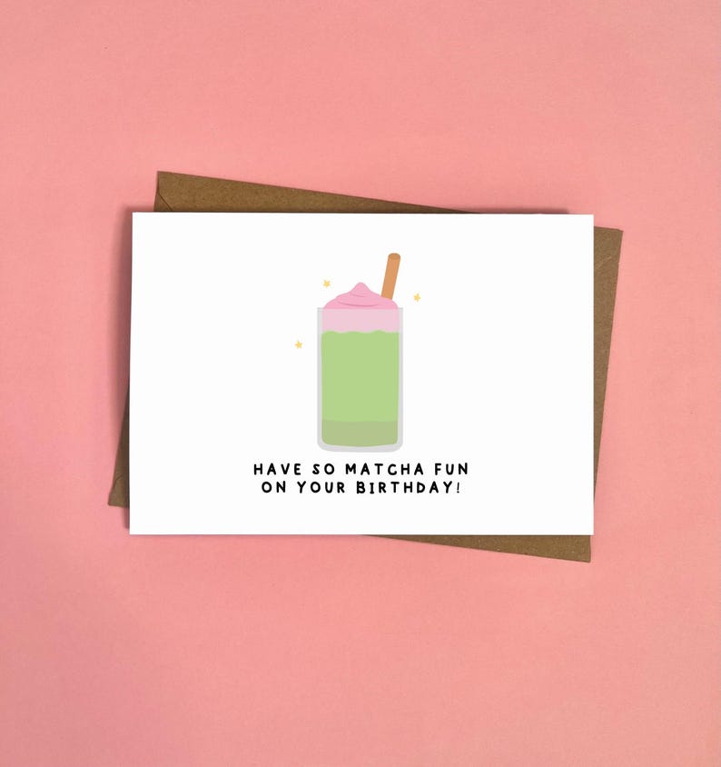 May include: A birthday greeting card with a matcha-themed illustration. The card features a green matcha drink with pink whipped cream and a straw. Text reads: "Have so matcha fun on your birthday!" The card is on a pink background.