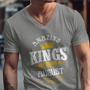 May include: A gray V-neck t-shirt with the text "AMAZING KINGS ARE BORN IN AUGUST" in white and yellow. The design includes a yellow crown above the word "KINGS".