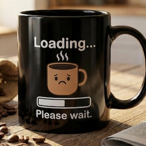 Peut inclure: Mug noir en céramique avec le texte "Loading... Please wait." et un dessin de tasse à café triste. Le mug est posé sur une surface en bois avec des grains de café et un sac en toile de jute.